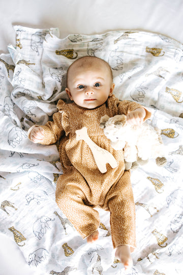 baby model laying down on animal patterned blanket, wearing giraffe onesie with giraffe shaped wood teether 