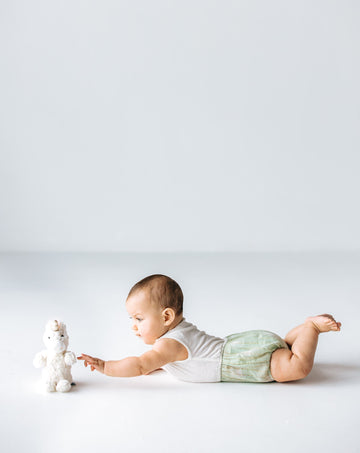 baby model laying on tummy reaching for unicorn plushie