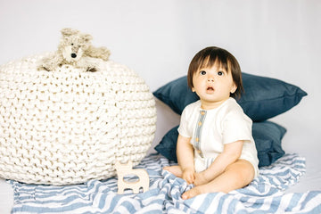 baby boy modeling white onesie with dog plushie and dog shaped wood teether