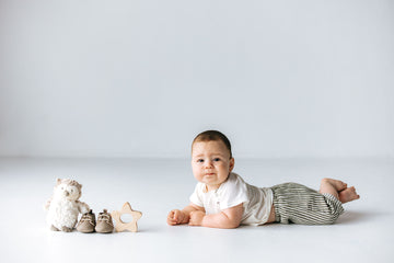 baby model laying on tummy with owl plushie, star wood teether, and shoes