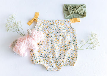 flatlay photo of pink pig plushie, yellow floral bubble romper and sage green headband